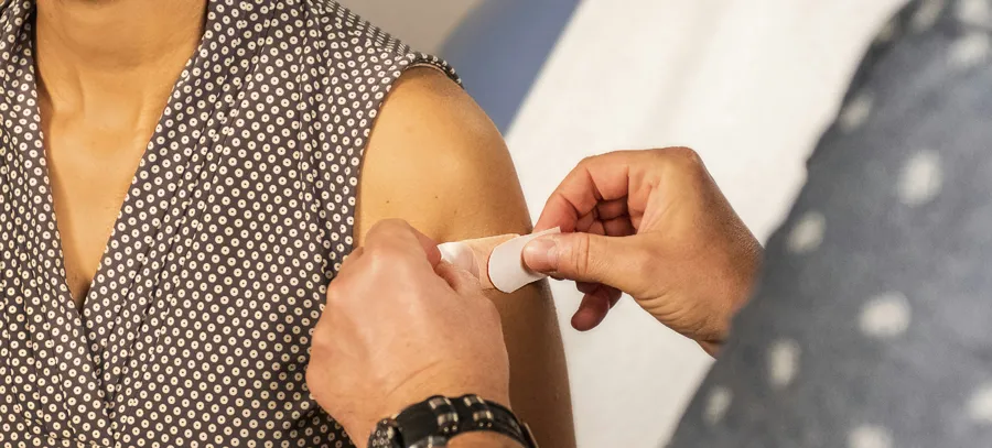 A medical professional places a bandage on a vaccine injection site