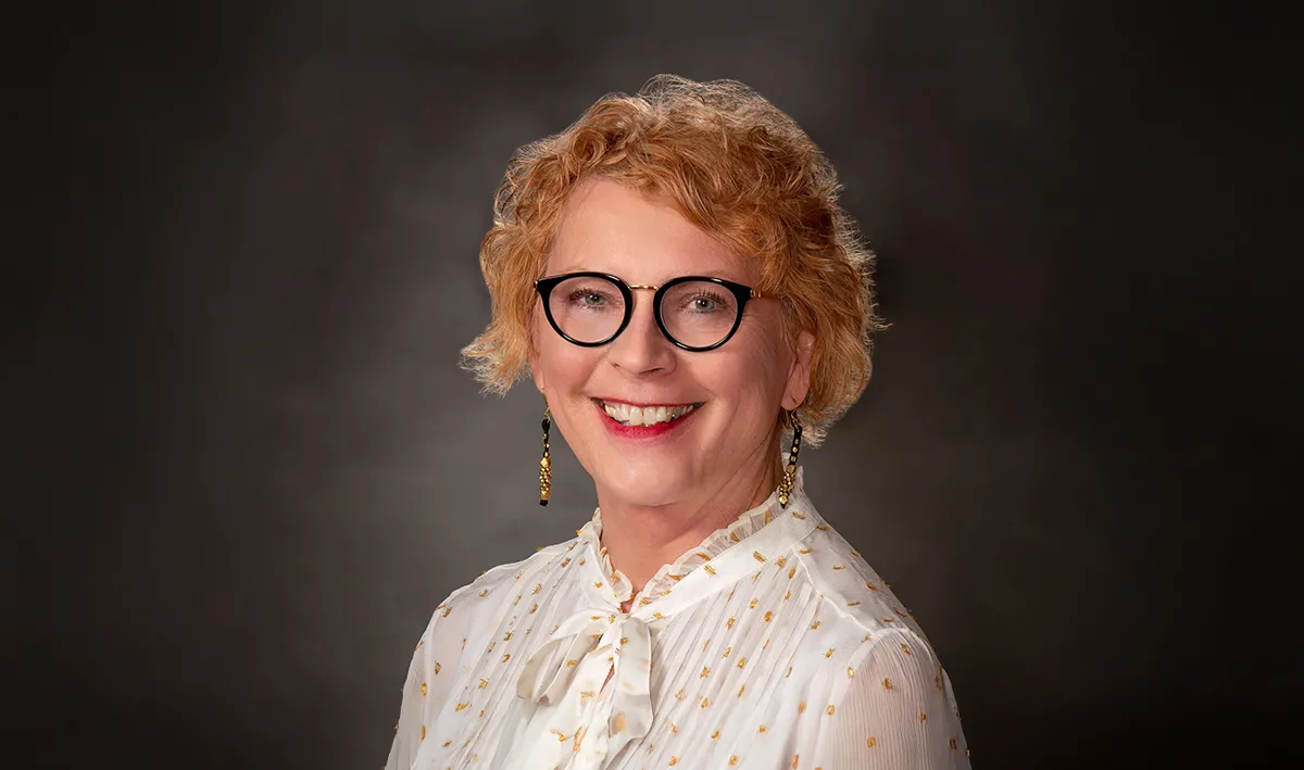 A portrait of a smiling caucasian woman with short red hair and wearing glasses