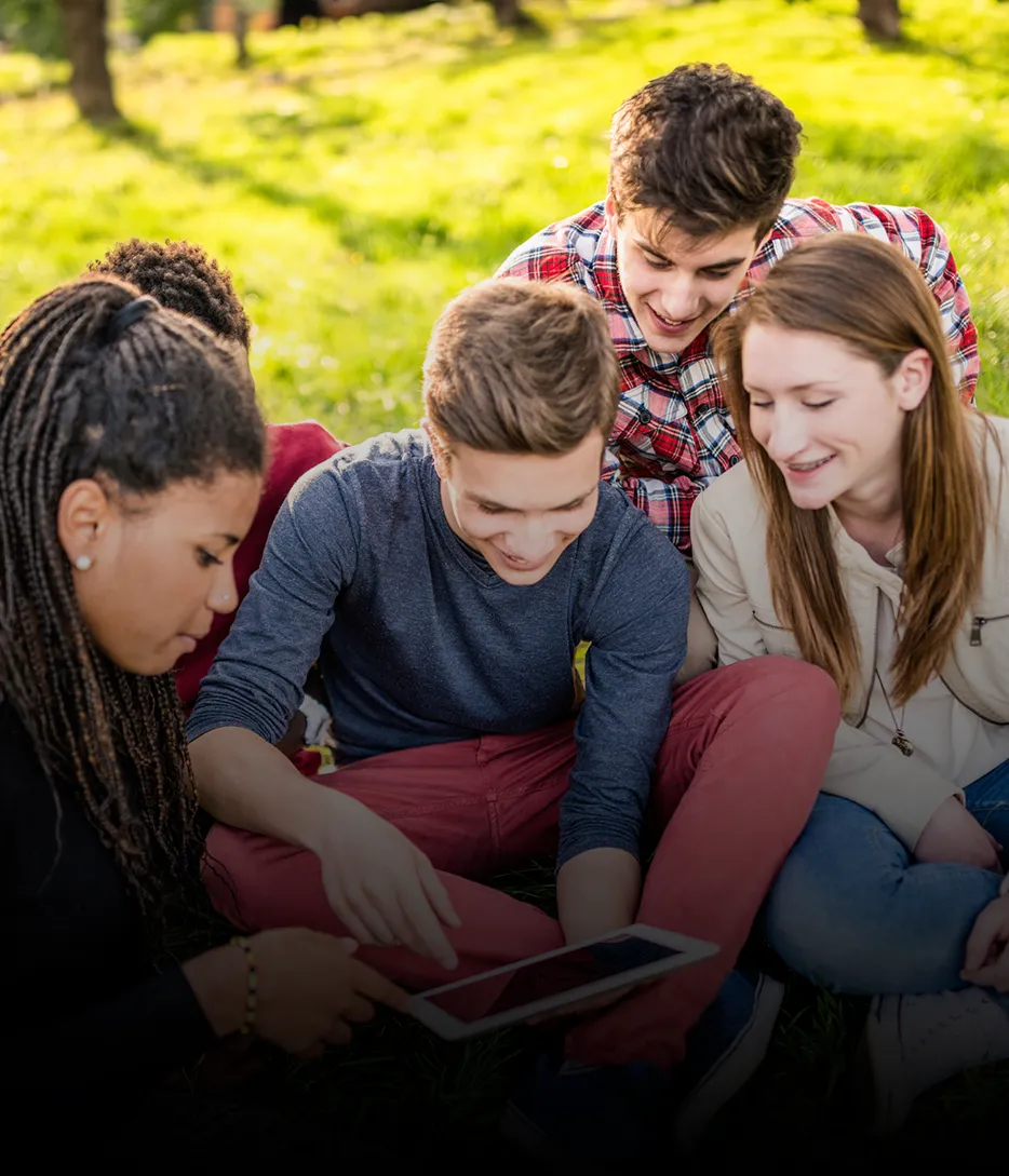 Four students look at a tablet together on the lawn in summer