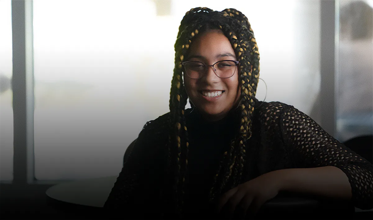 A young, smiling African American woman with long braids and glasses