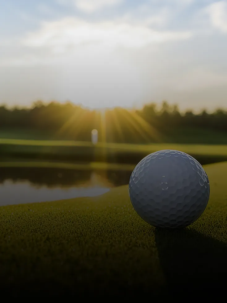 A closeup of a golf ball resting on a golf course next to a pond