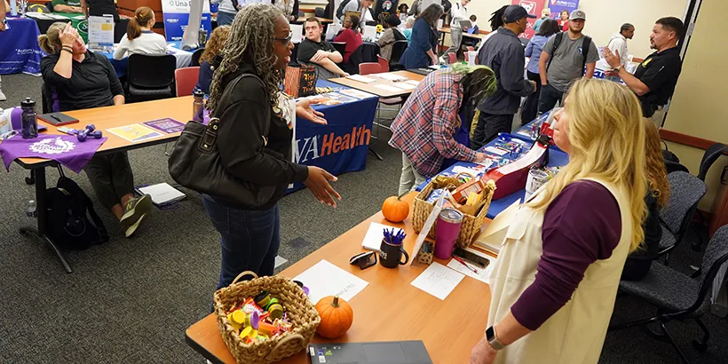 A woman stops by a table at a career fair to ask a vendor questions about their employment opportunities