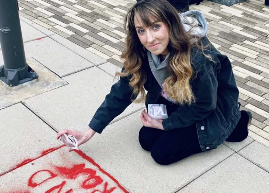 A participant pours red sand into sidewalk cracks as part of the Red Sand Project, an art initiative designed to raise awareness of human trafficking