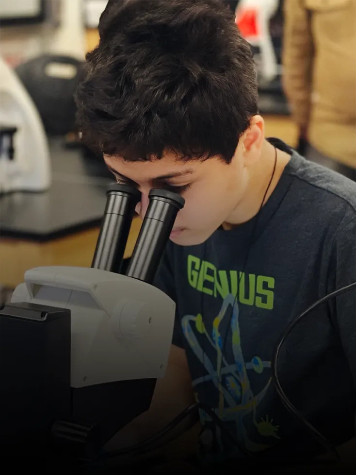 A young boy looks into a microscope in a science lab