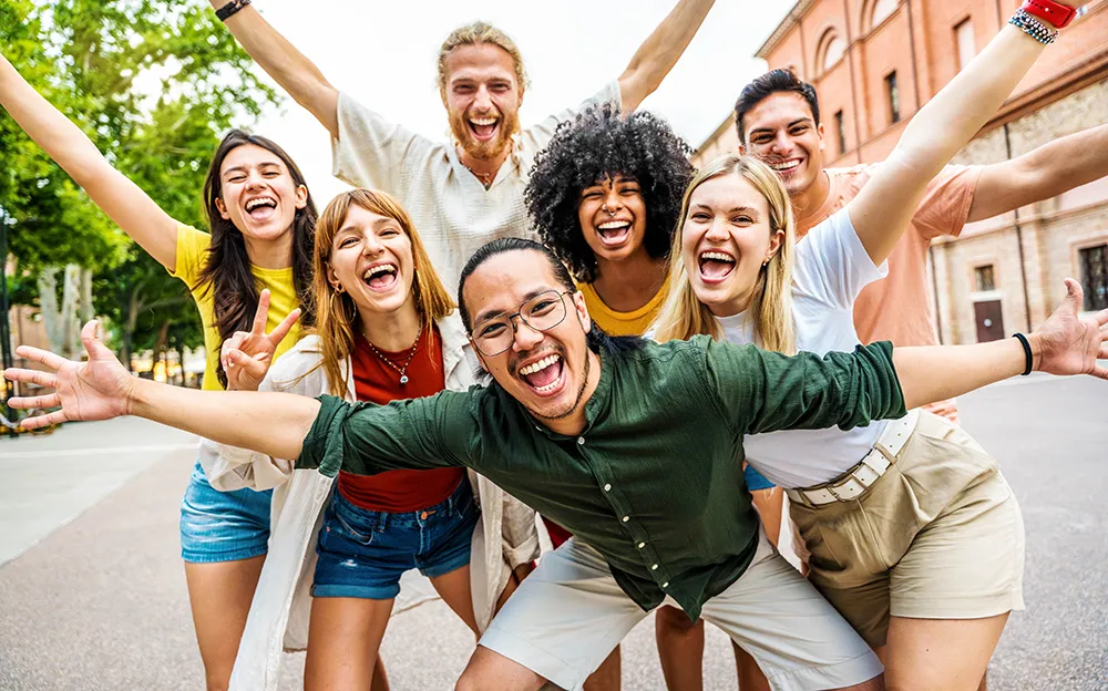 Seven grinning college students throw their hands in the air as they pose for a photo