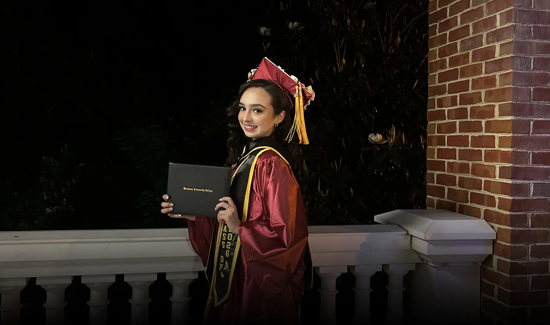 Nathaly Zaragoza, in a graduation cap and gown, proudly holds up her diploma at Germanna's Commencement ceremony