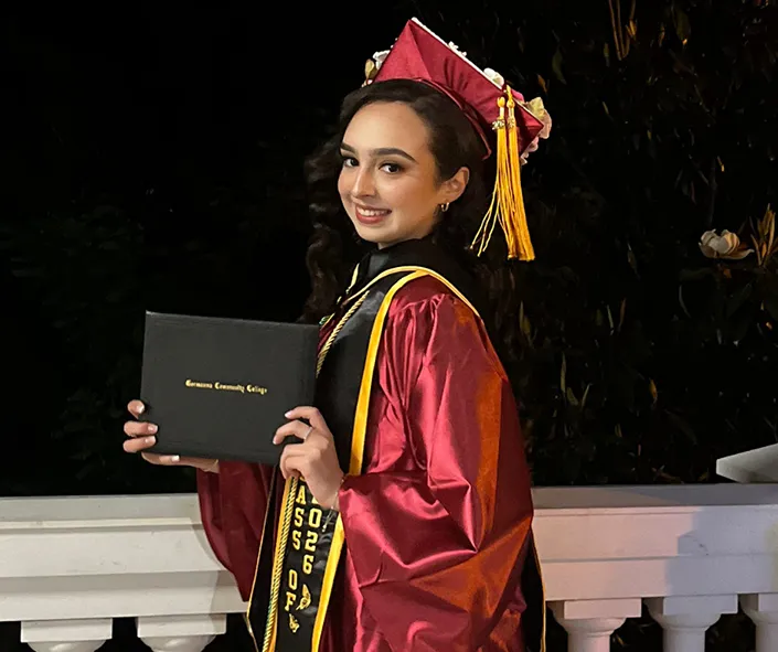 Nathaly Zaragoza, in a graduation cap and gown, proudly holds up her diploma at Germanna's Commencement ceremony