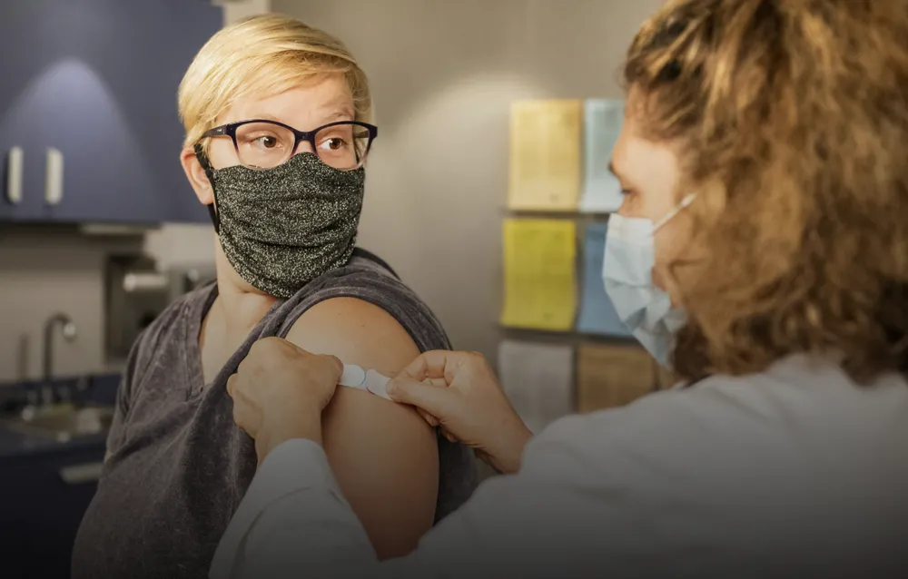A woman in a face mask receiving a vaccine from a medical professional