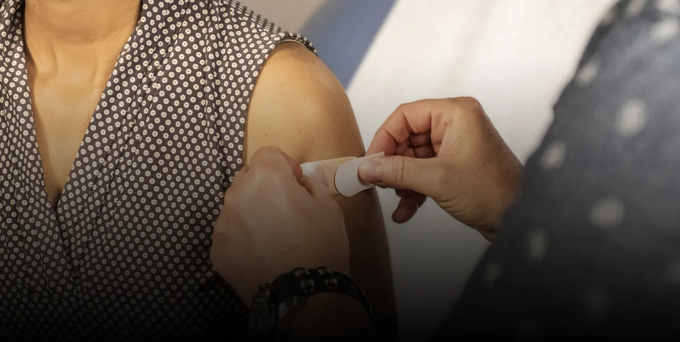 A nurse applies a band-aid to a patient's arm after administering a vaccine