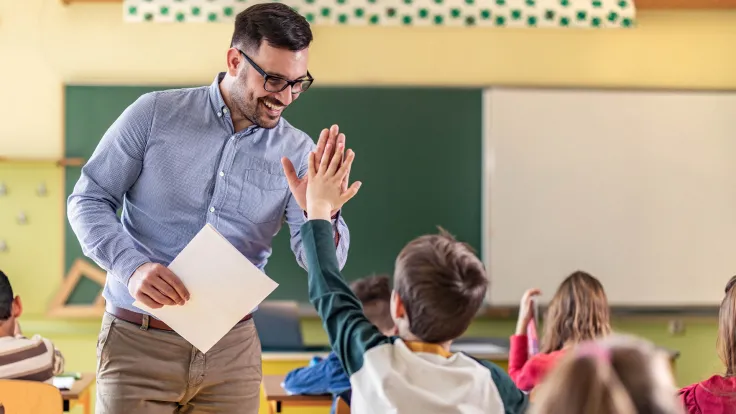 Teacher in a elementary school classroom giving one of his students a high five