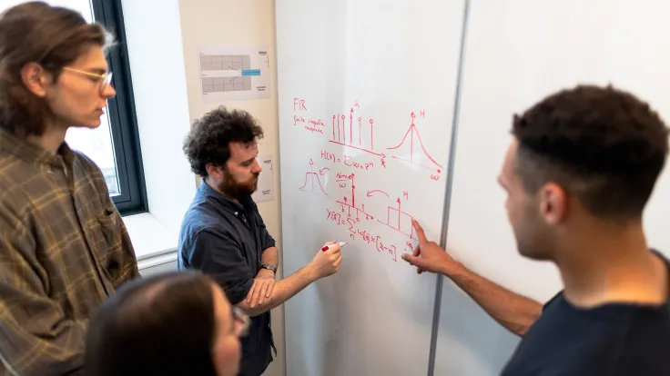 A Group of College Age Math Students Working to Solve an Equation on a White Board