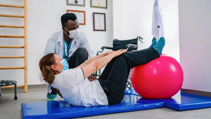 Adult woman with trainer doing rehab using pilates ball in the rehabilitation center