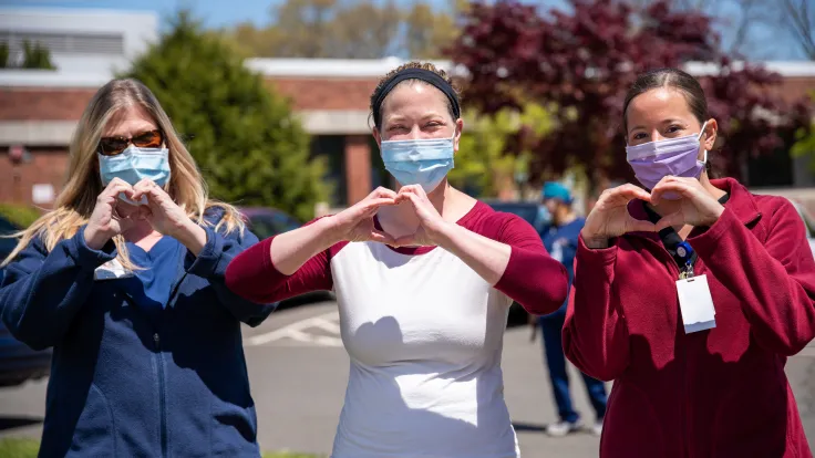 Three female nurses holding up heart hands outside