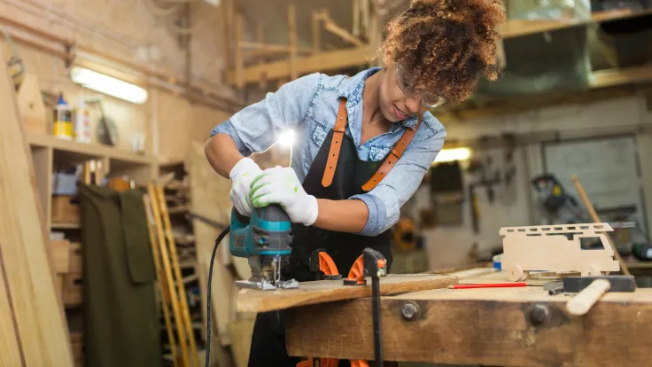 A woman drills into a plank of wood in a carpentry shop