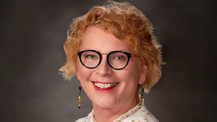 A portrait of a smiling caucasian woman with short red hair and wearing glasses