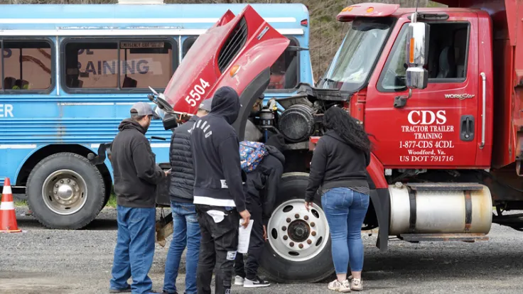 Students look inside the hood of a commercial truck during CDL training