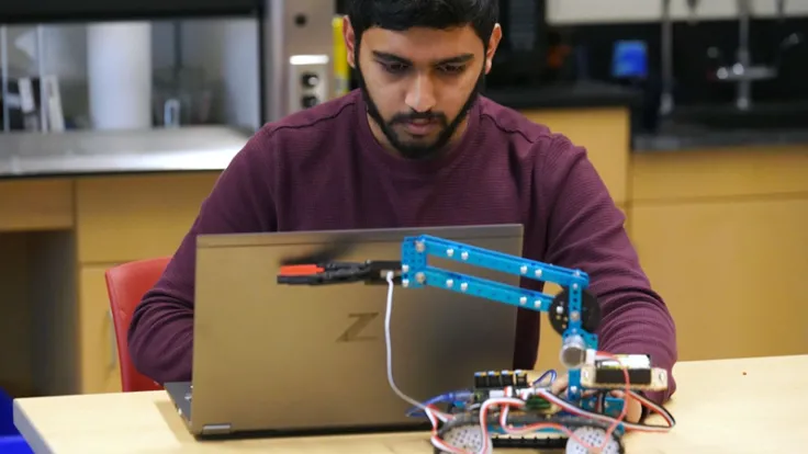 A student works on a laptop to program a robot