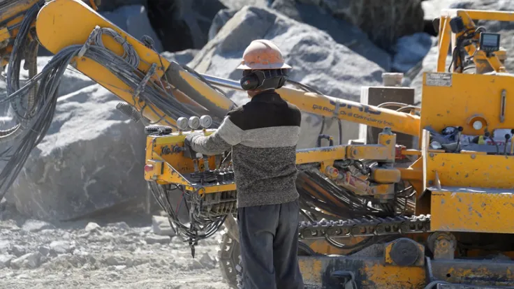 A worker operates large construction machinery at a stone quarry
