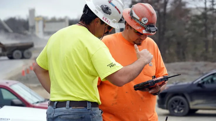 Two heavy equipment operators discuss ongoing construction work at a stone quarry
