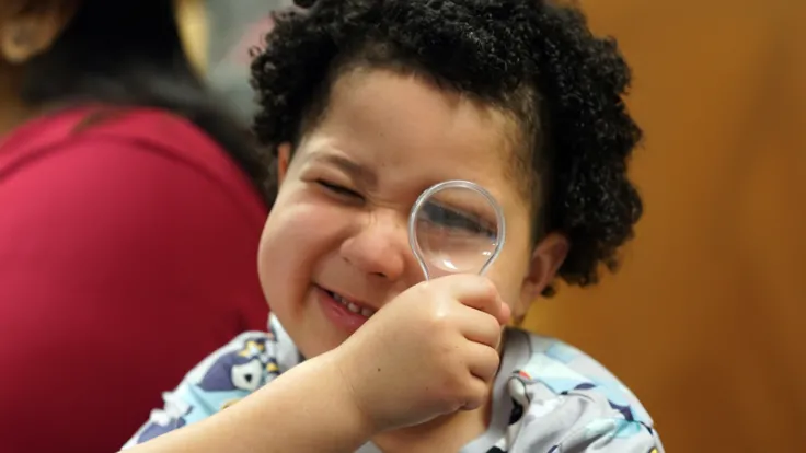 A young child squints to look through a magnifying glass