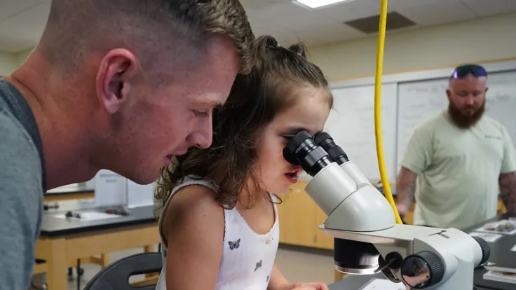 A teacher observes a child looking through a microscope