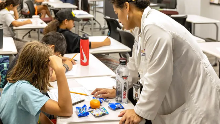 A woman wearing a lab coat helps a young student in the classroom