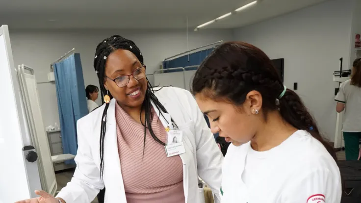 A nursing faculty member guides a student in a lab setting