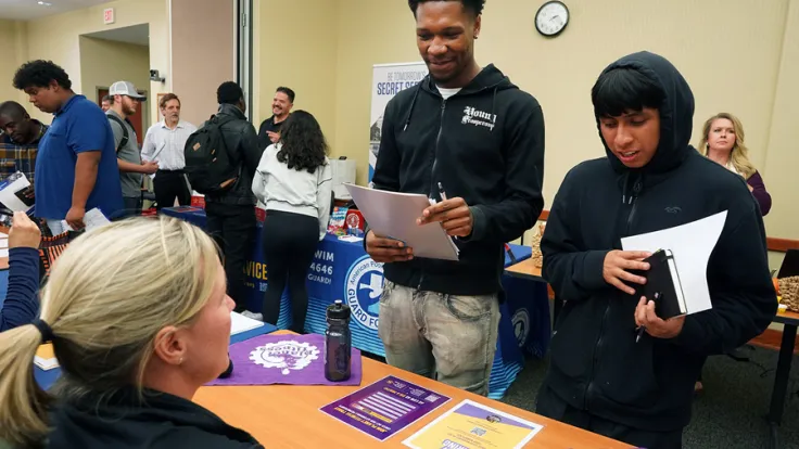 Students ask an employer questions at a table during a career fair