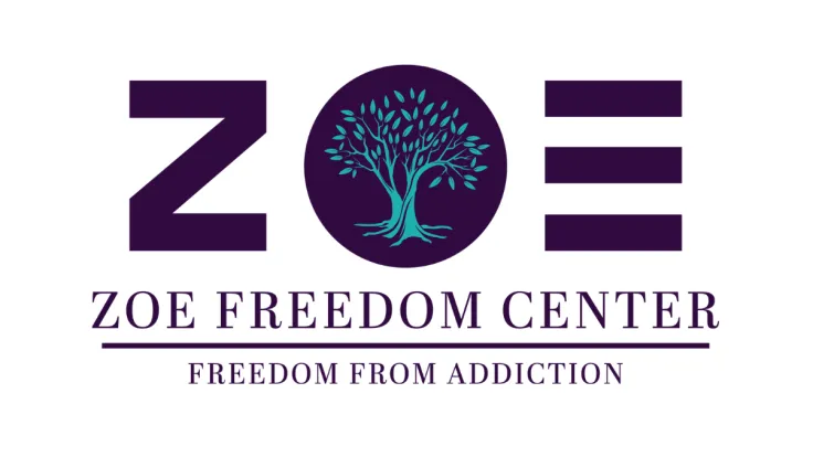 The logo for Zoe Freedom Center. Purple lettering with a leafy green tree filling the center of the 'O'. The text reads: "Zoe Freedom Center—Freedom From Addiction"