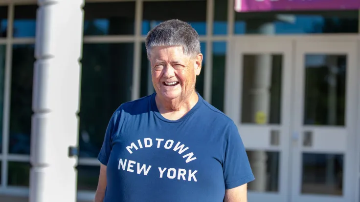 A smiling man in a blue t-shirt that reads "Midtown New York"