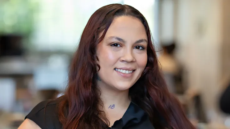 A smiling young woman with long brown hair wearing a black whirt