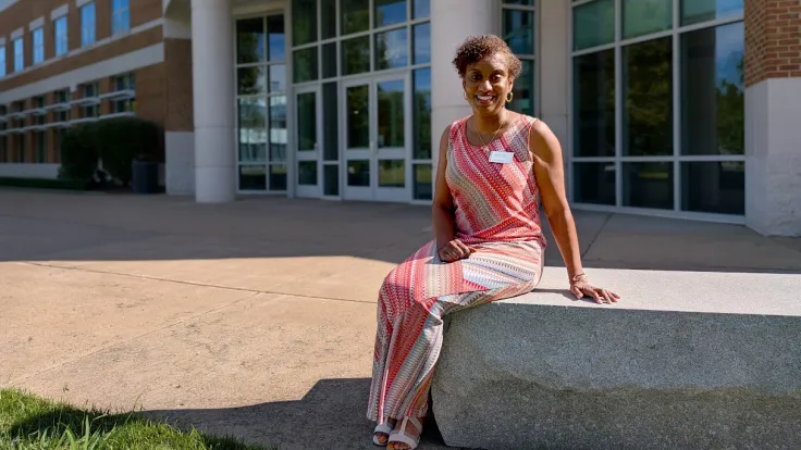 A woman in a coral print dress poses for a photo on the Germanna campus