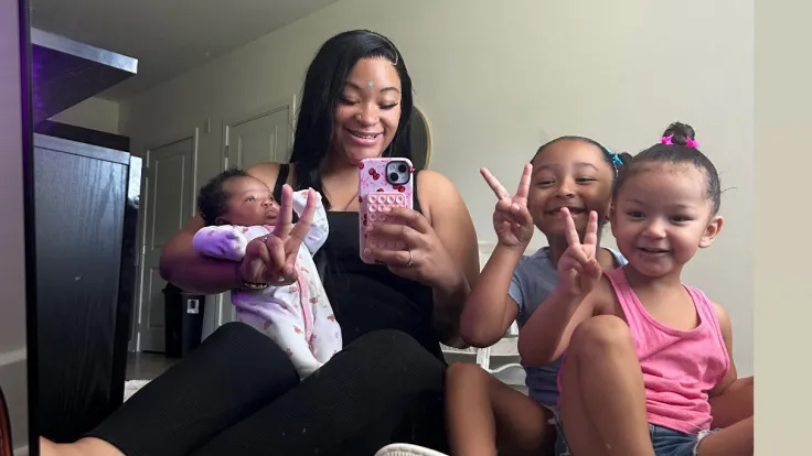 A young woman takes a selfie with her three young children in their living room