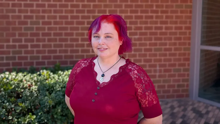 Brandy Fallon, Germanna Adjunct Professor, poses in front of a campus building wearing a vibrant red dress